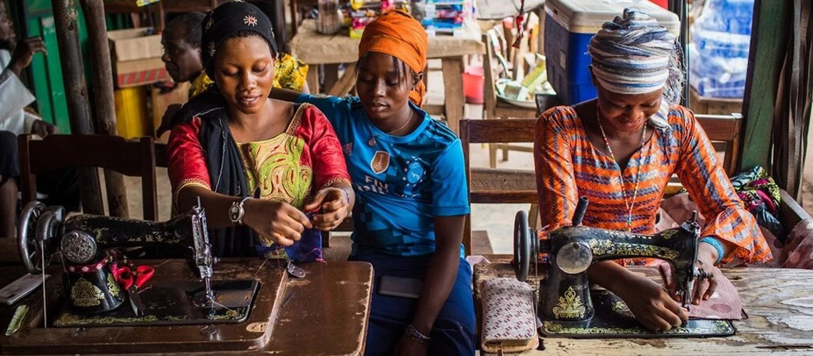 Young women sewing clothes in a market in Boké, Guinea. Photo credit: Vincent Tremeau / World Bank.